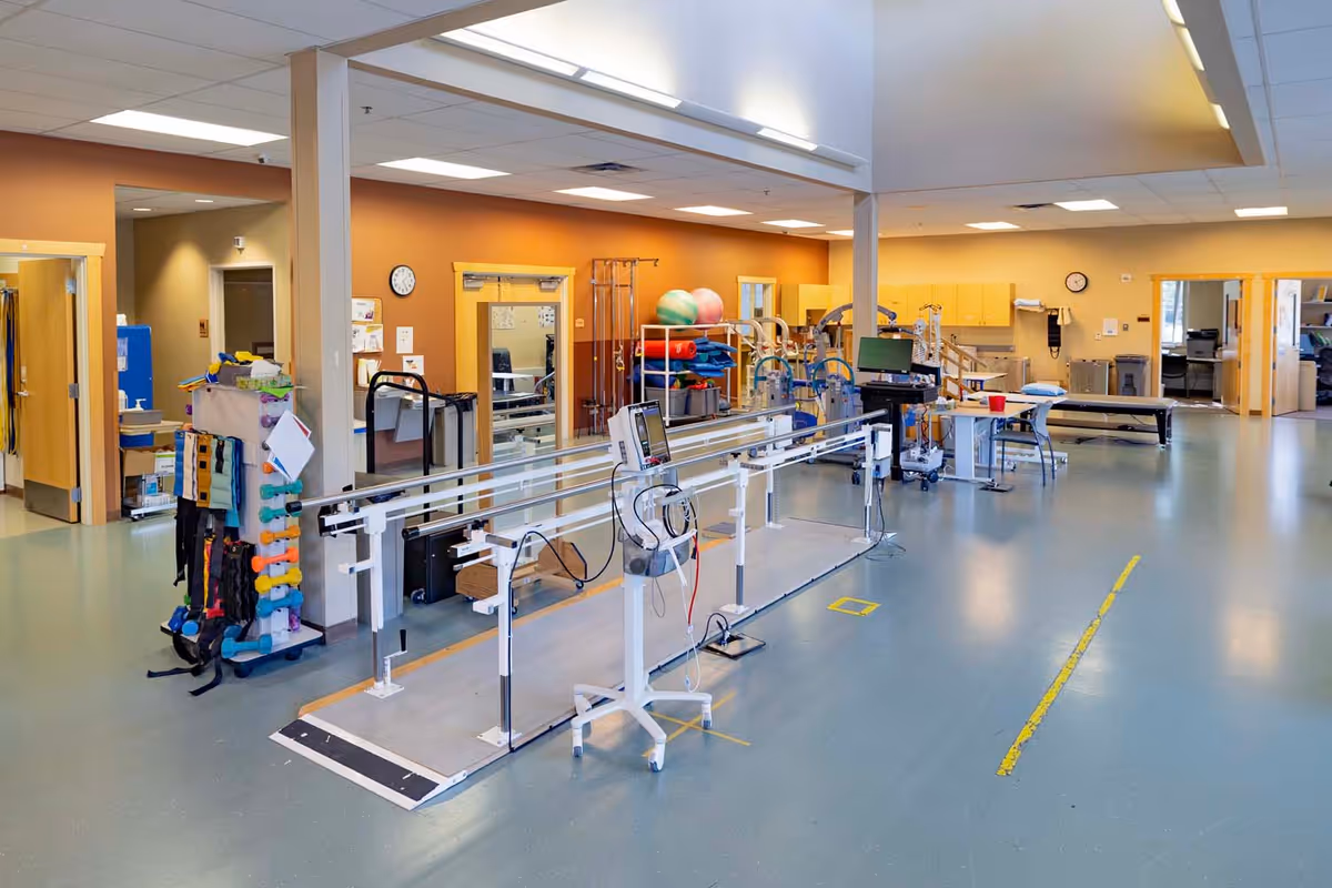 Bright rehabilitation gym with parallel bars, therapy equipment, and exercise balls in a senior care facility.