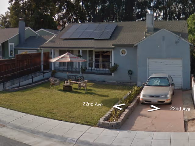 A single-story blue senior living home with a front lawn, outdoor seating, and a parked car.