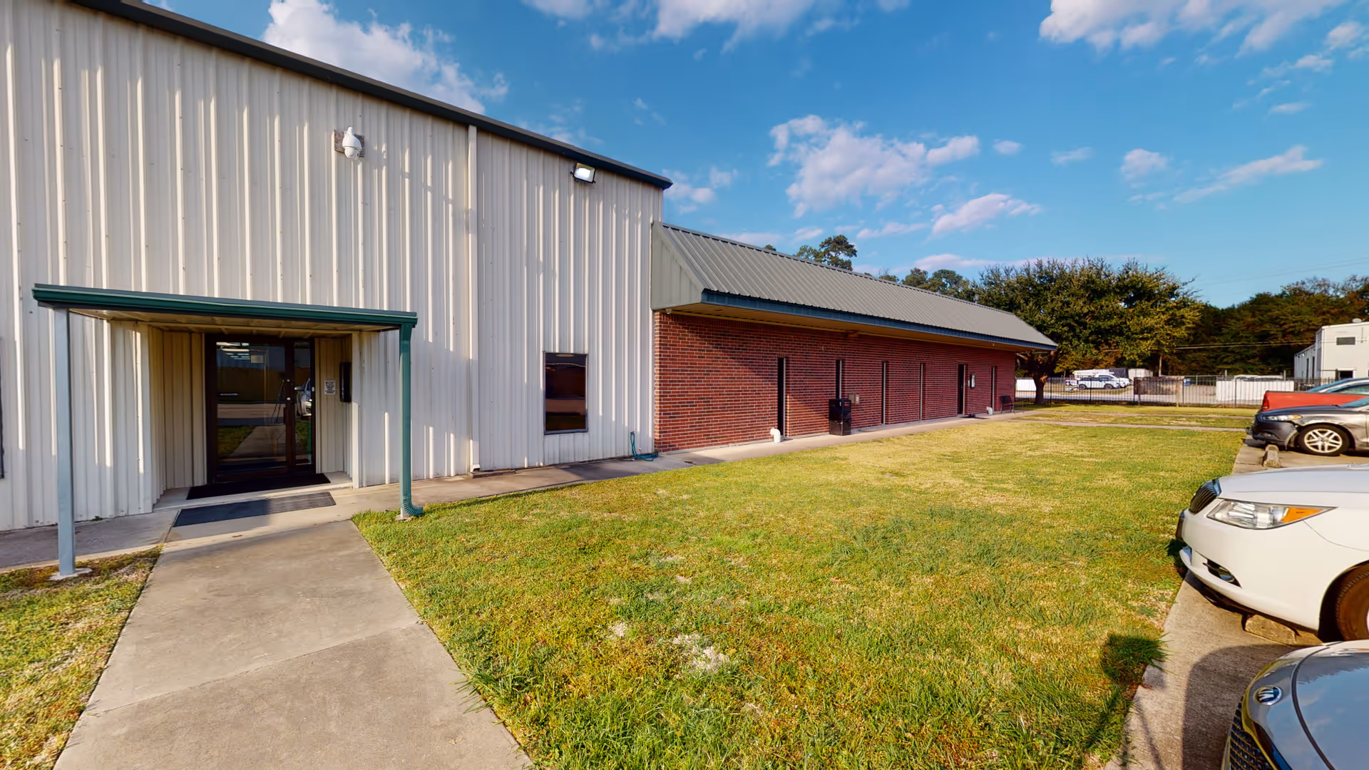 Exterior view of a building entrance with sidewalk and parked cars.