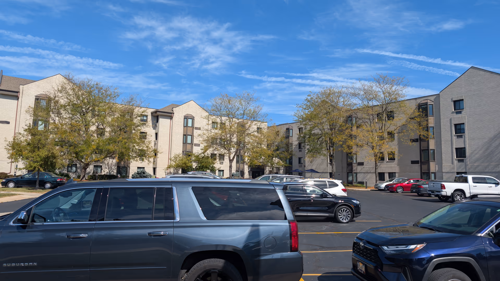 Exterior view of Harbour House senior living buildings with parked cars and blue sky.