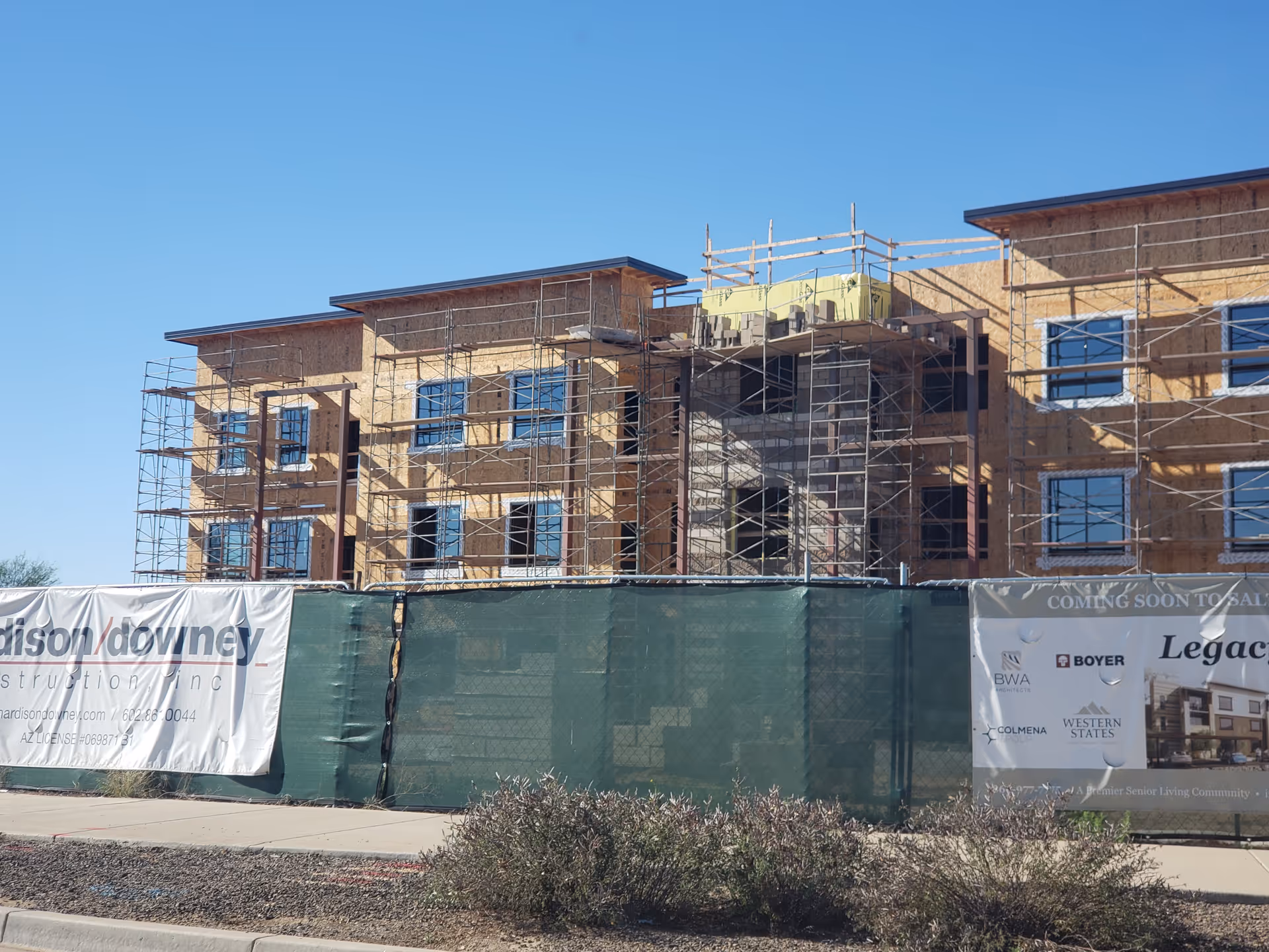 Front of a multi-story building under construction with scaffolding and banners.