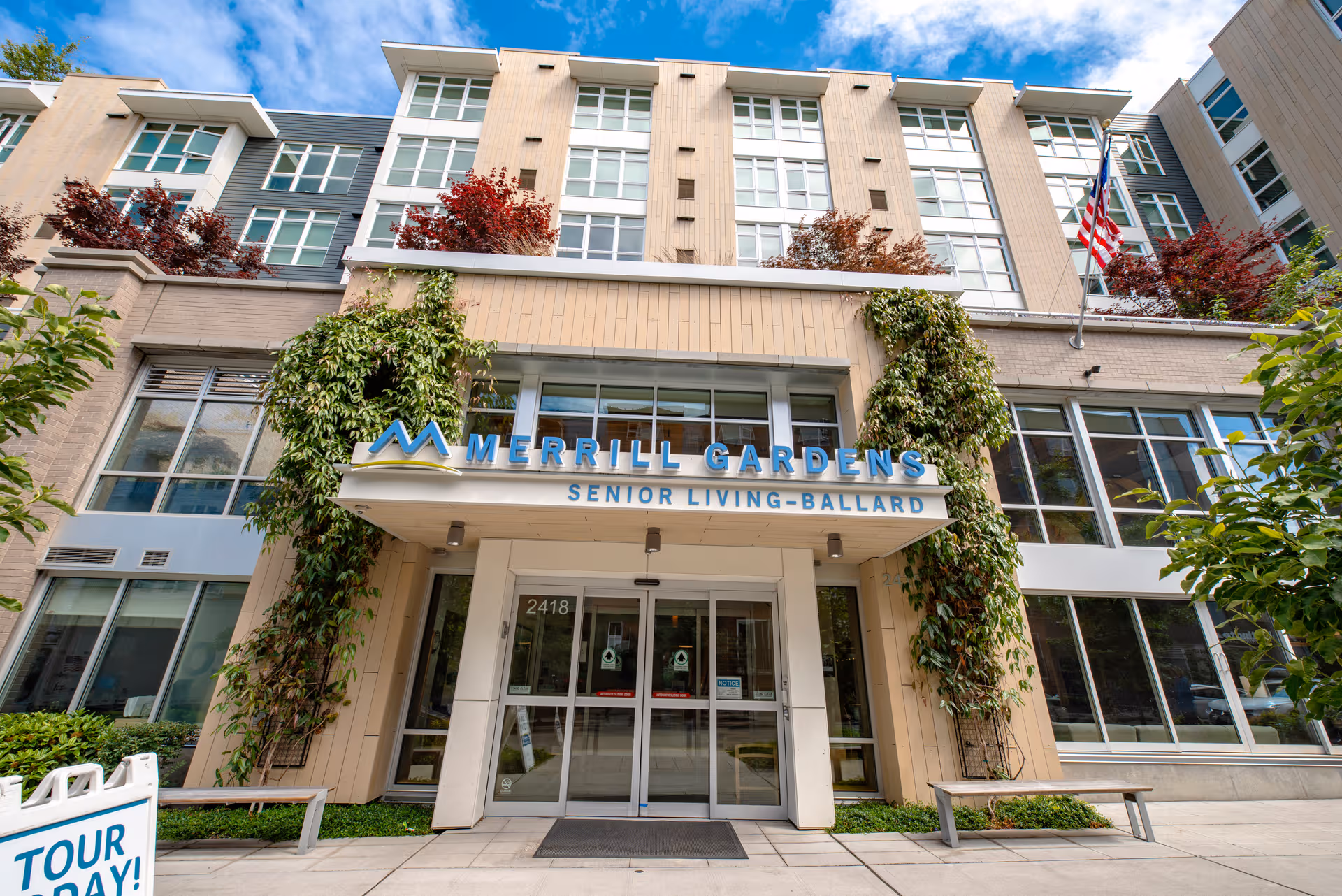 Merrill Gardens at Ballard exterior building entrance with sign and greenery