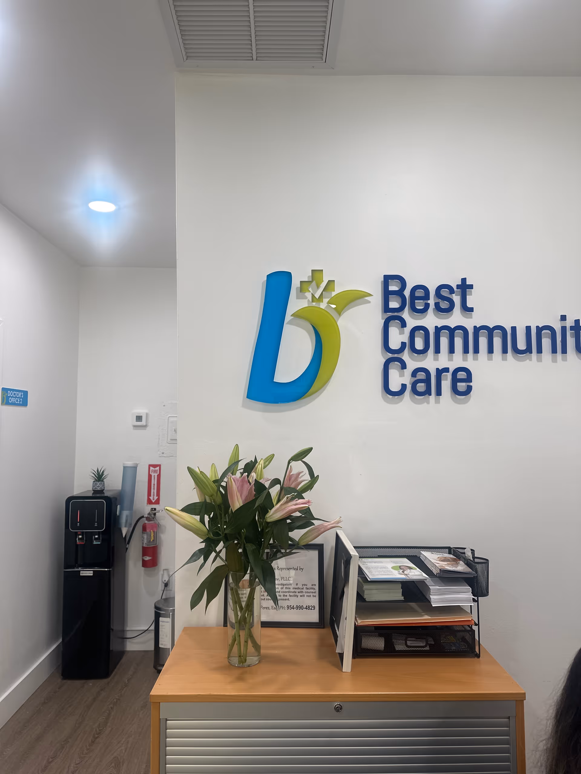 Reception area with Best Community Care sign, flowers, brochures, and water cooler.