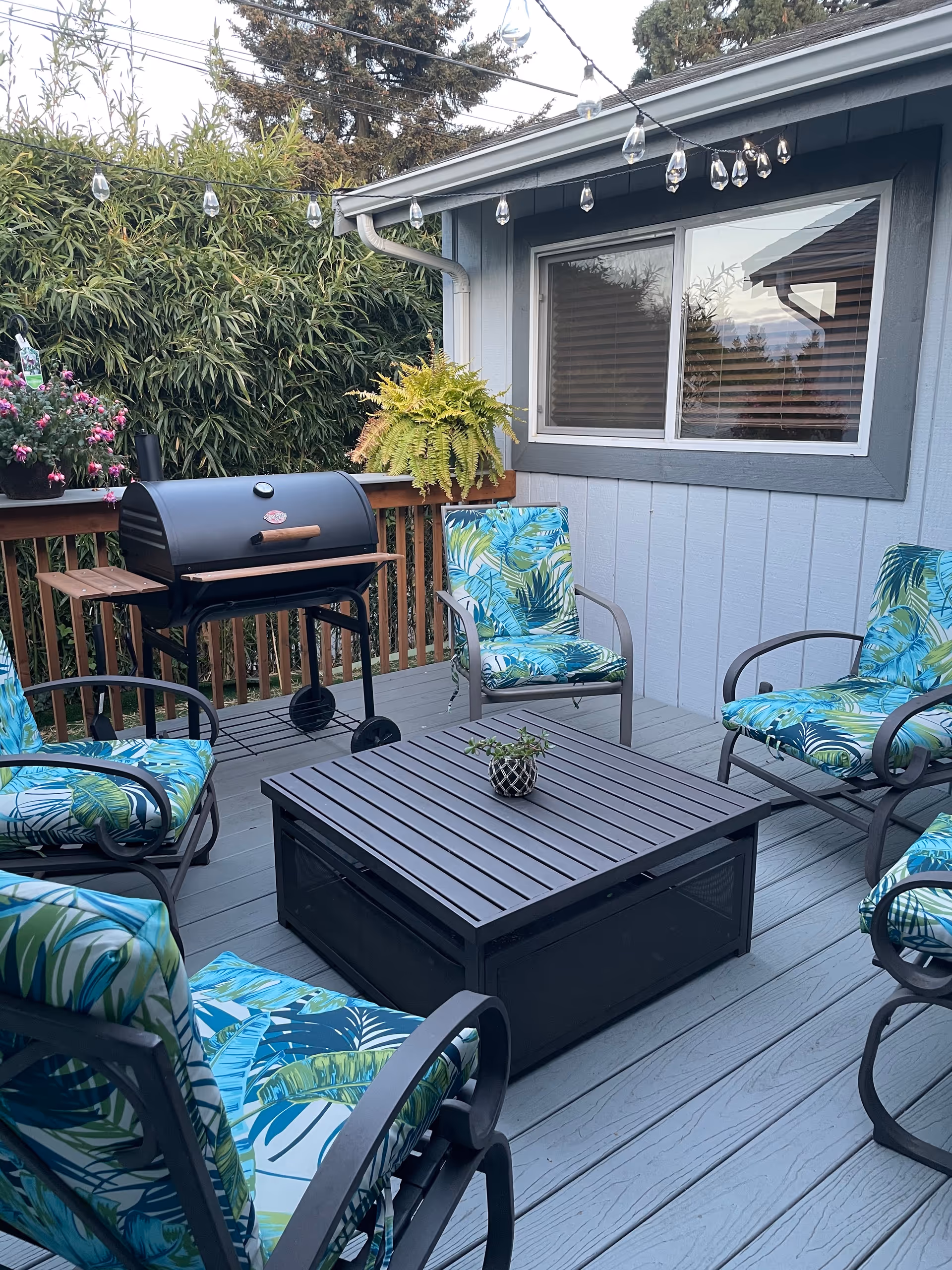 Outdoor patio at a senior care facility with tropical chairs, a grill, and string lights.