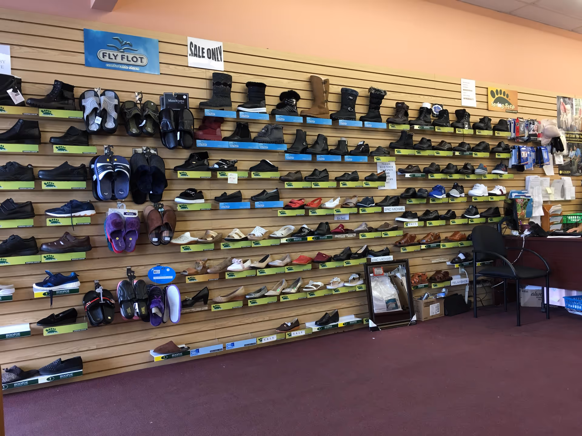 Indoor shoe store display with many shoes on slatwall shelves.