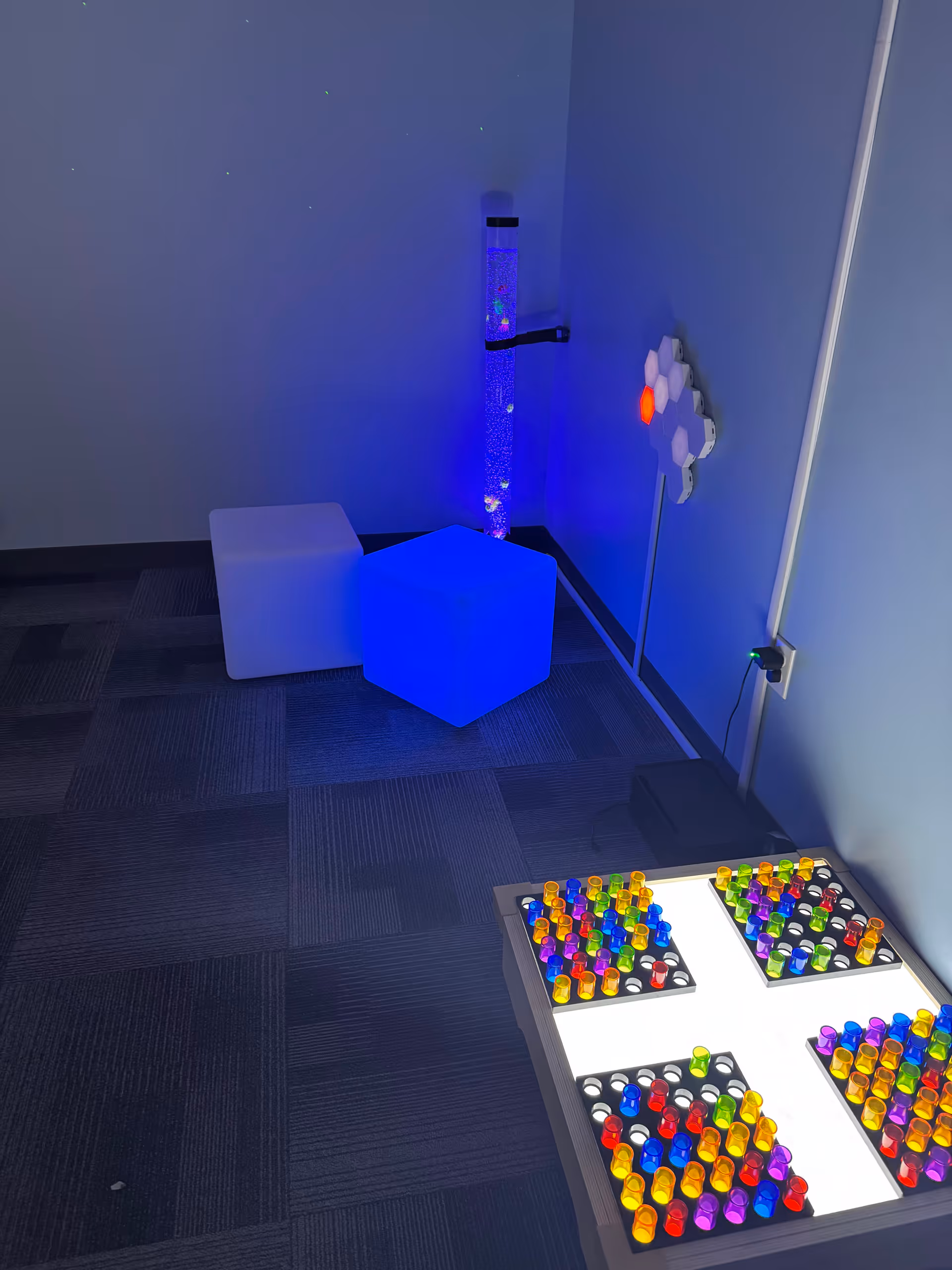 Sensory therapy room with bubble tube, illuminated cubes, and a lighted peg table.