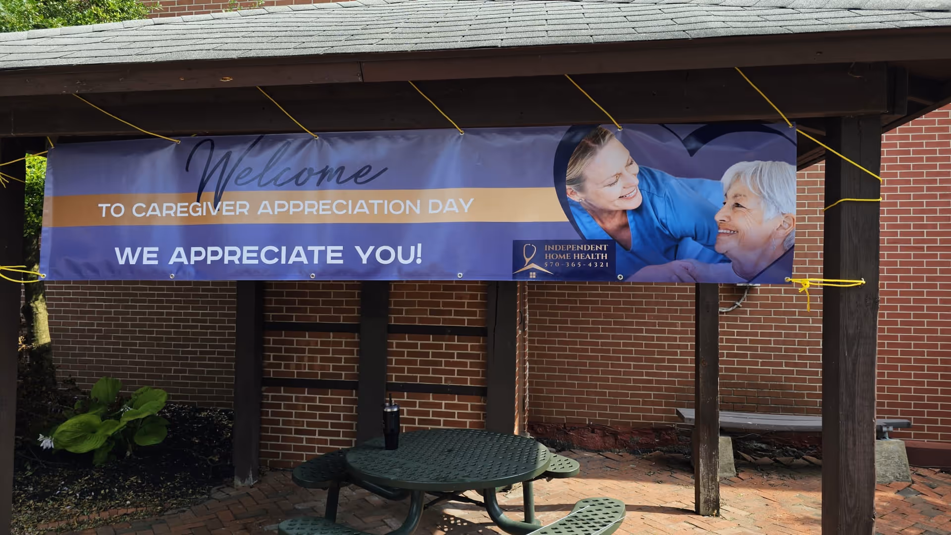 Banner under a wooden shelter outside a brick wall with a picnic table nearby.