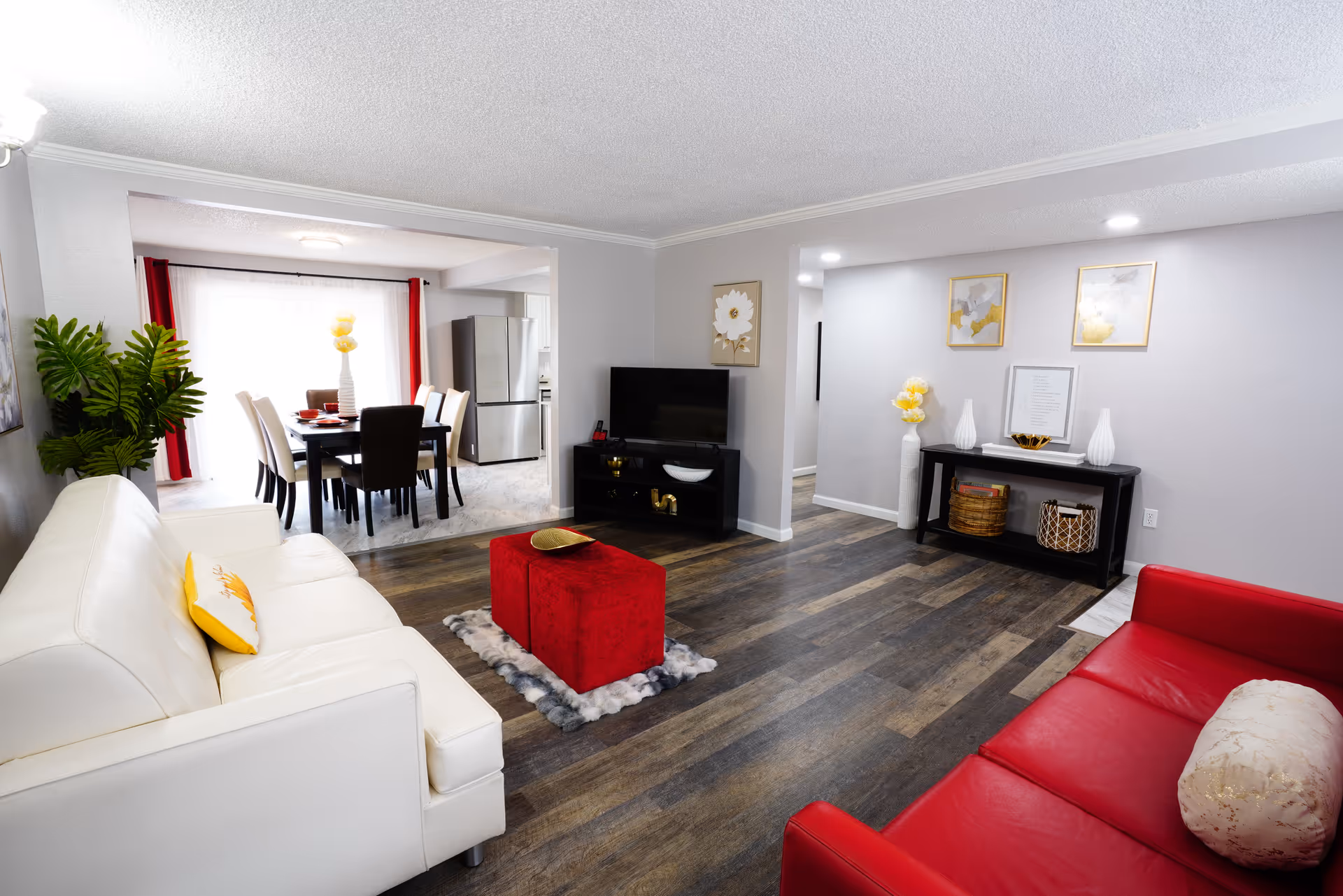 Modern living room with white sofa, red seating, coffee table, and adjacent dining area.