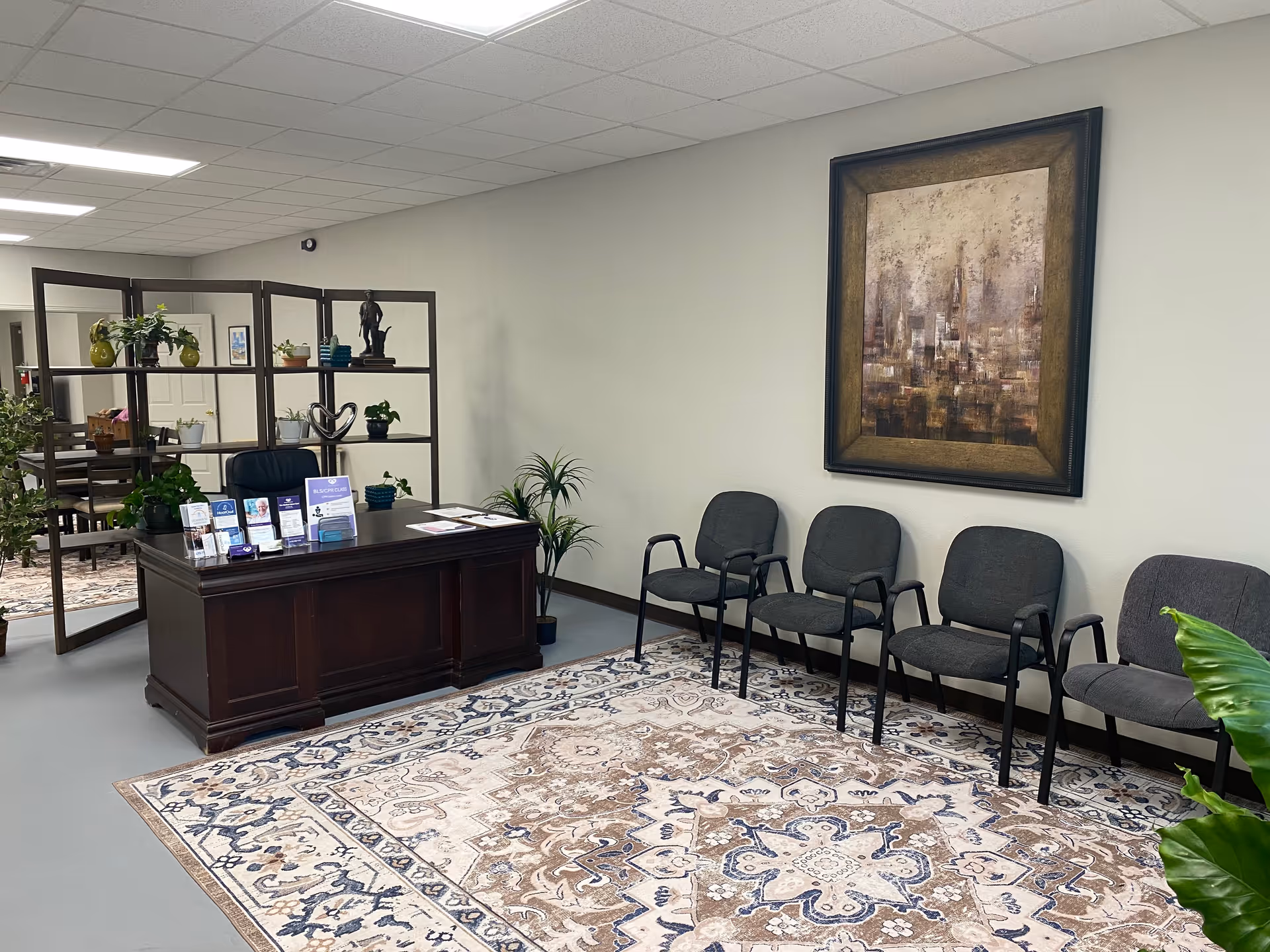 Reception desk in a lobby with chairs, plants, and a large wall painting.