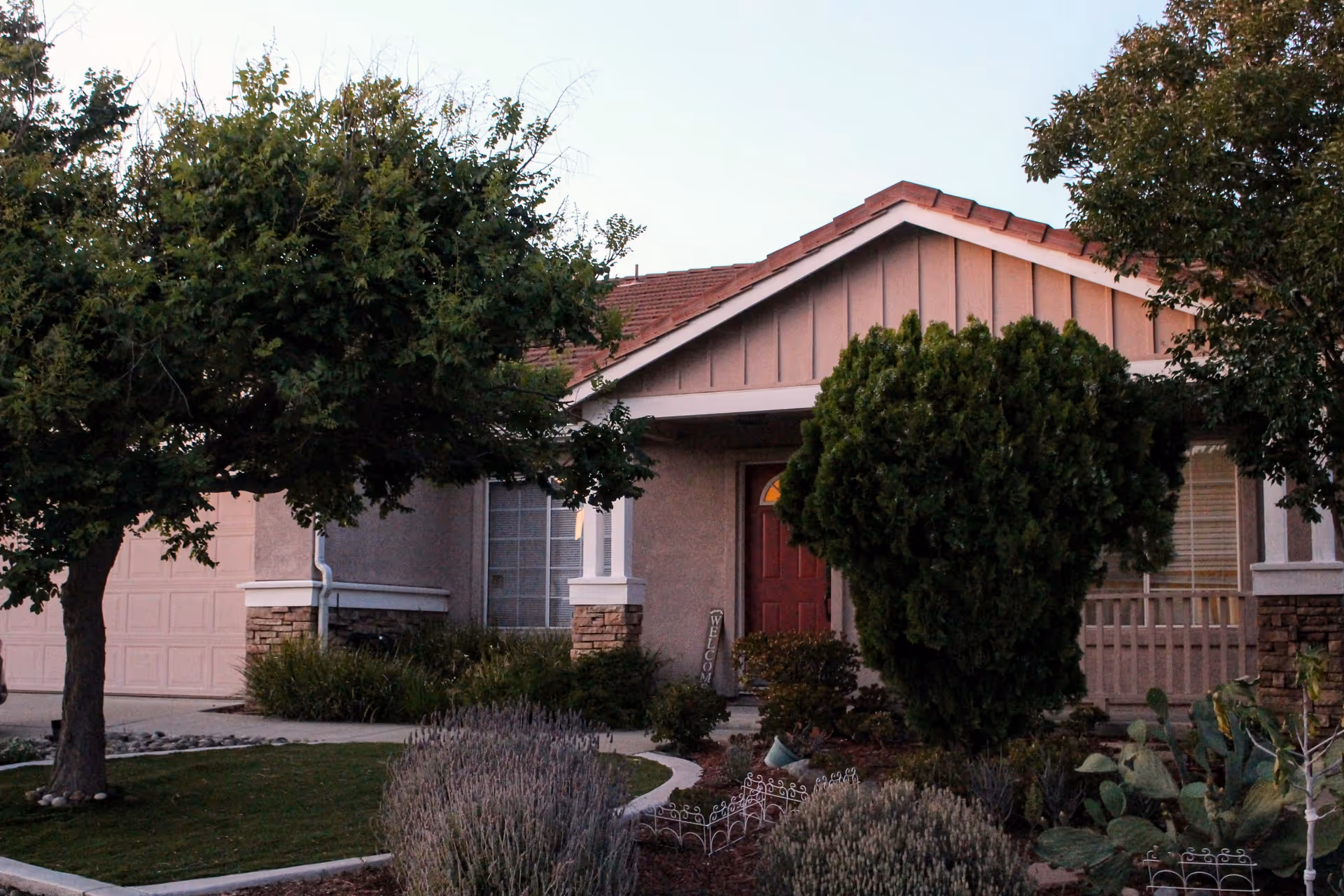 Front view of a pink, single-story senior care facility with trees and shrubs.