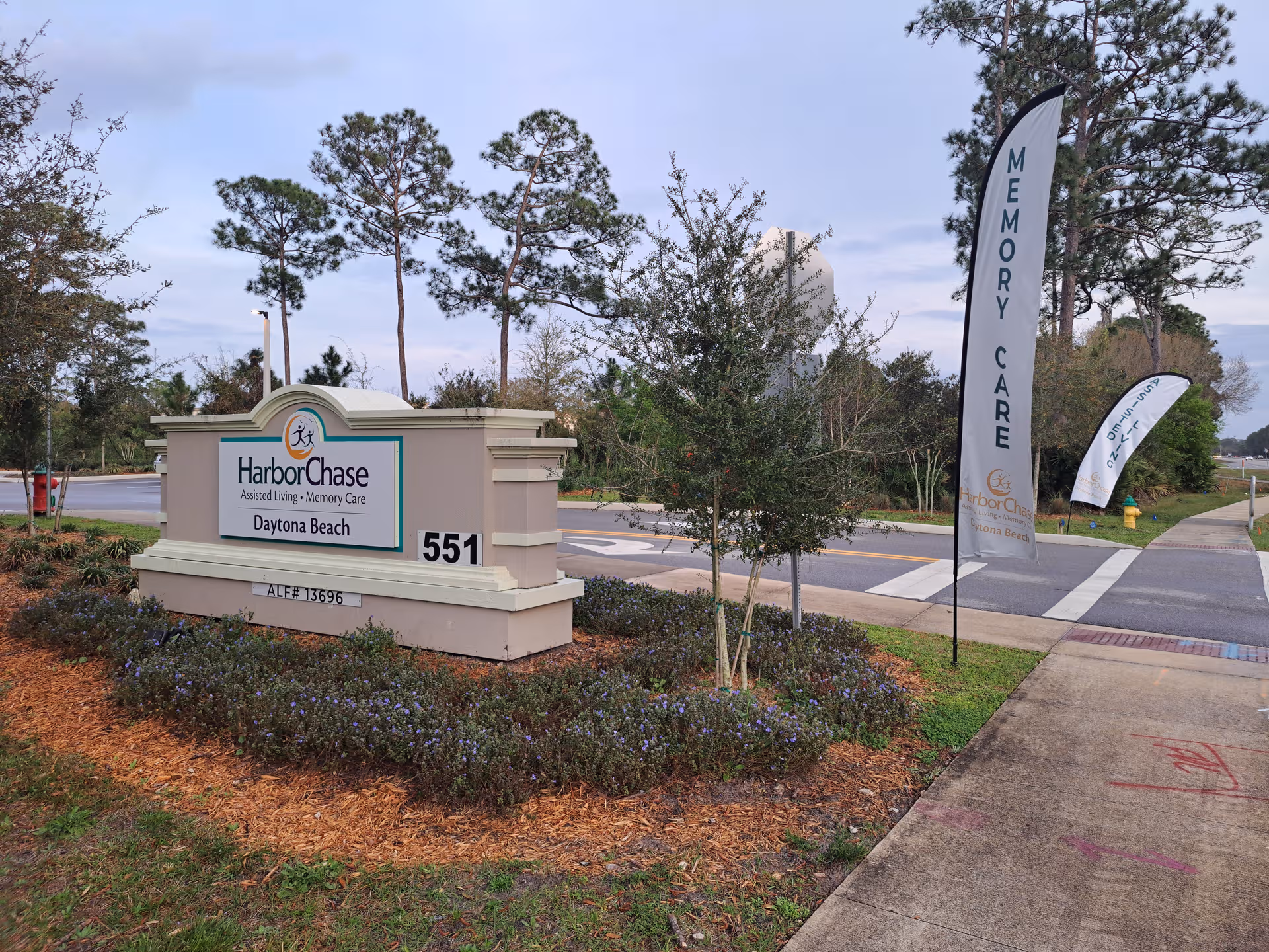 Entrance sign for HarborChase of Daytona Beach with landscaping and tall trees.