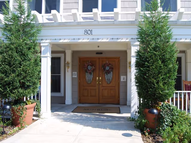 Entrance with double wooden doors and wreaths, flanked by white columns at Sunrise of Staten Island.