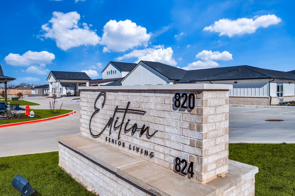 Exterior view of Edition Senior Living facility with brick sign and surrounding drive, buildings in background.