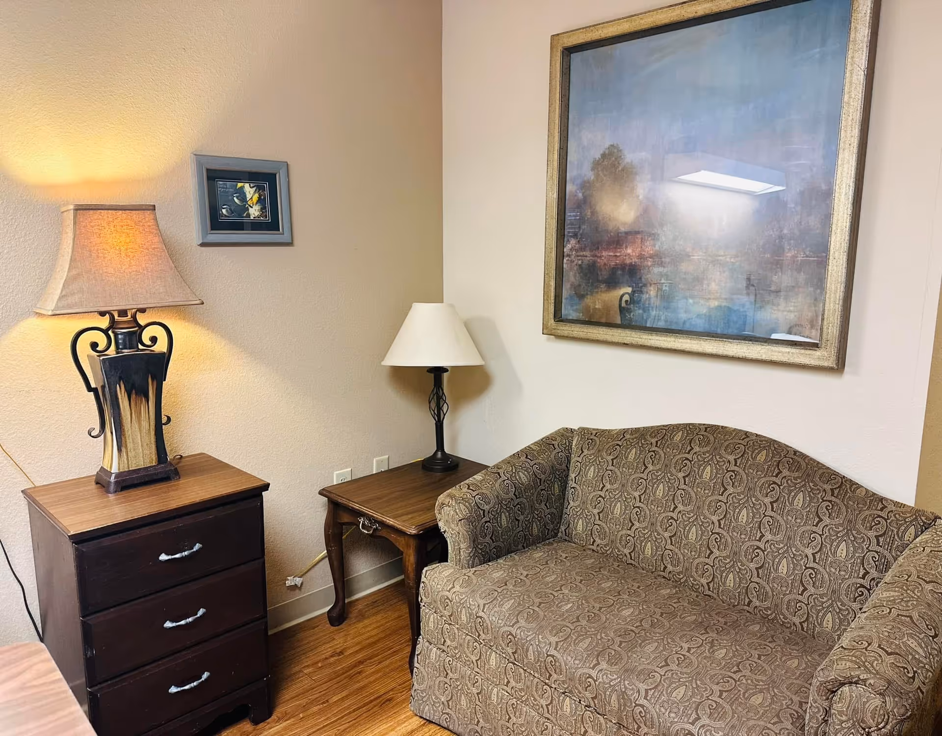 Cozy living room in a senior facility with sofa, lamps, tables, and wall art.