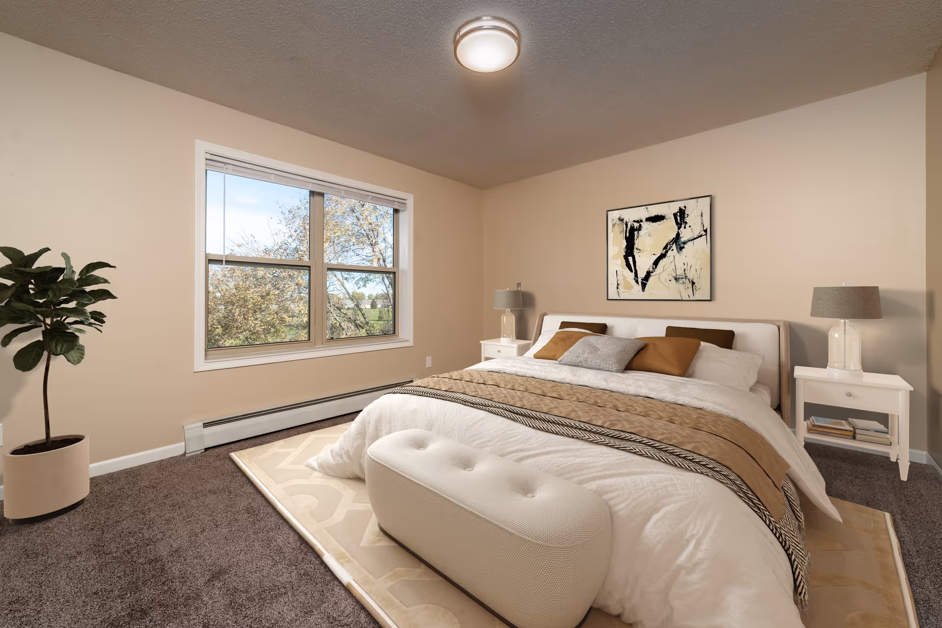 A cozy bedroom with a large bed featuring white and beige bedding, multiple pillows, and a beige throw blanket. There is a white cushioned bench at the foot of the bed, two white nightstands with lamps on either side, a potted plant in the corner, a large window showing trees outside, and an abstract painting on the wall above the bed.