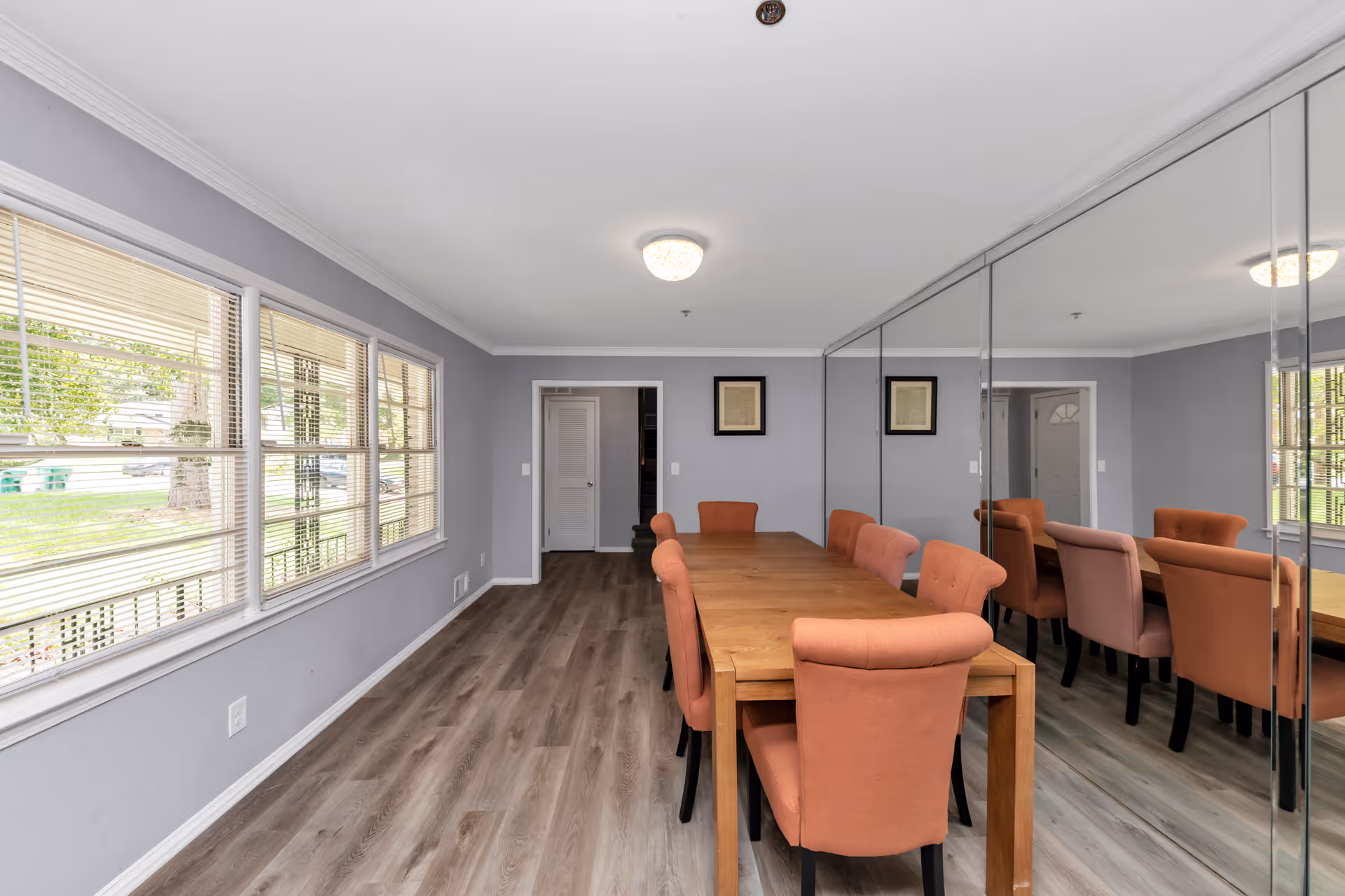 Bright dining room with a long wooden table and orange upholstered chairs along mirrored wall.