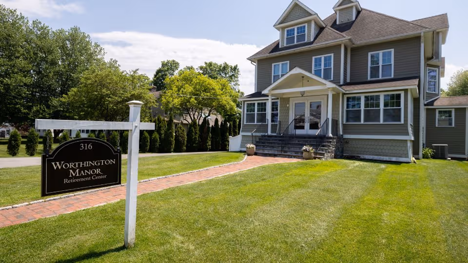 A large, multi-story retirement center with a manicured lawn and a sign reading Worthington Manor.