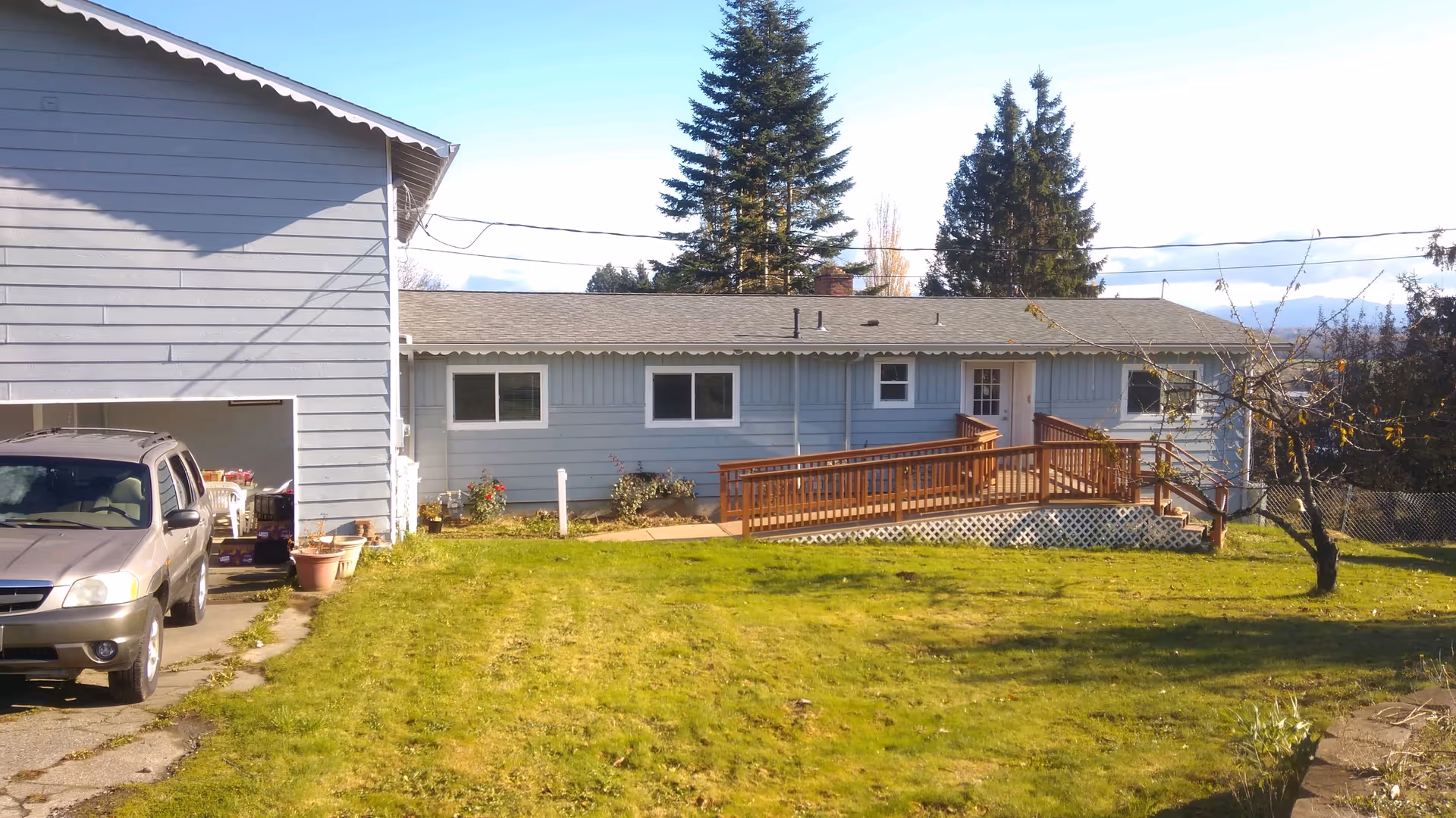 Single-story blue senior living home with a wooden ramp, deck, and lawn