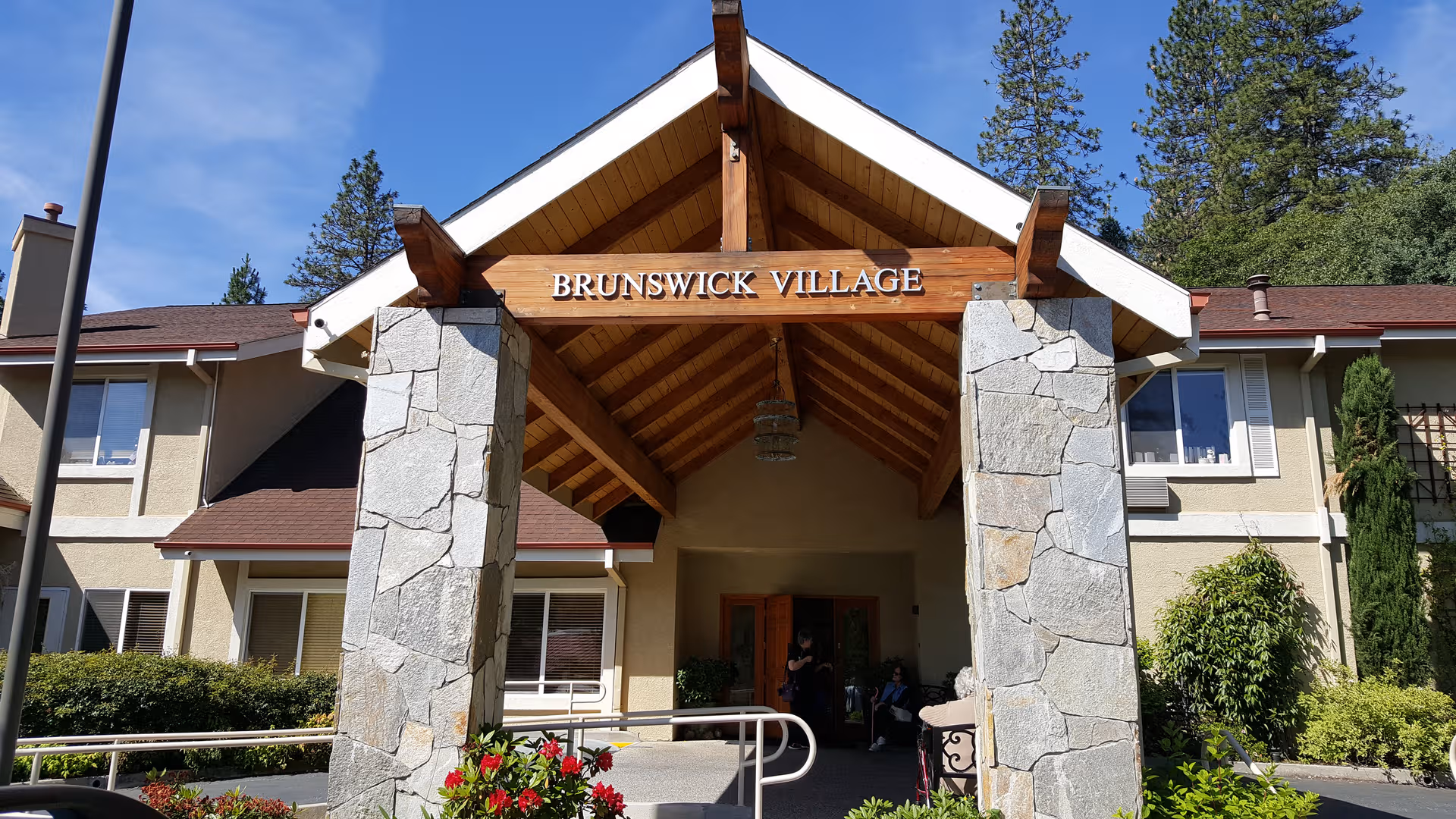 Entrance to Brunswick Village Assisted Living with stone pillars and a wooden peaked canopy.
