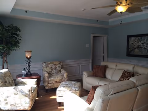 Light blue-walled living room with beige leather sofa, patterned chairs, ottoman, and ceiling fan.