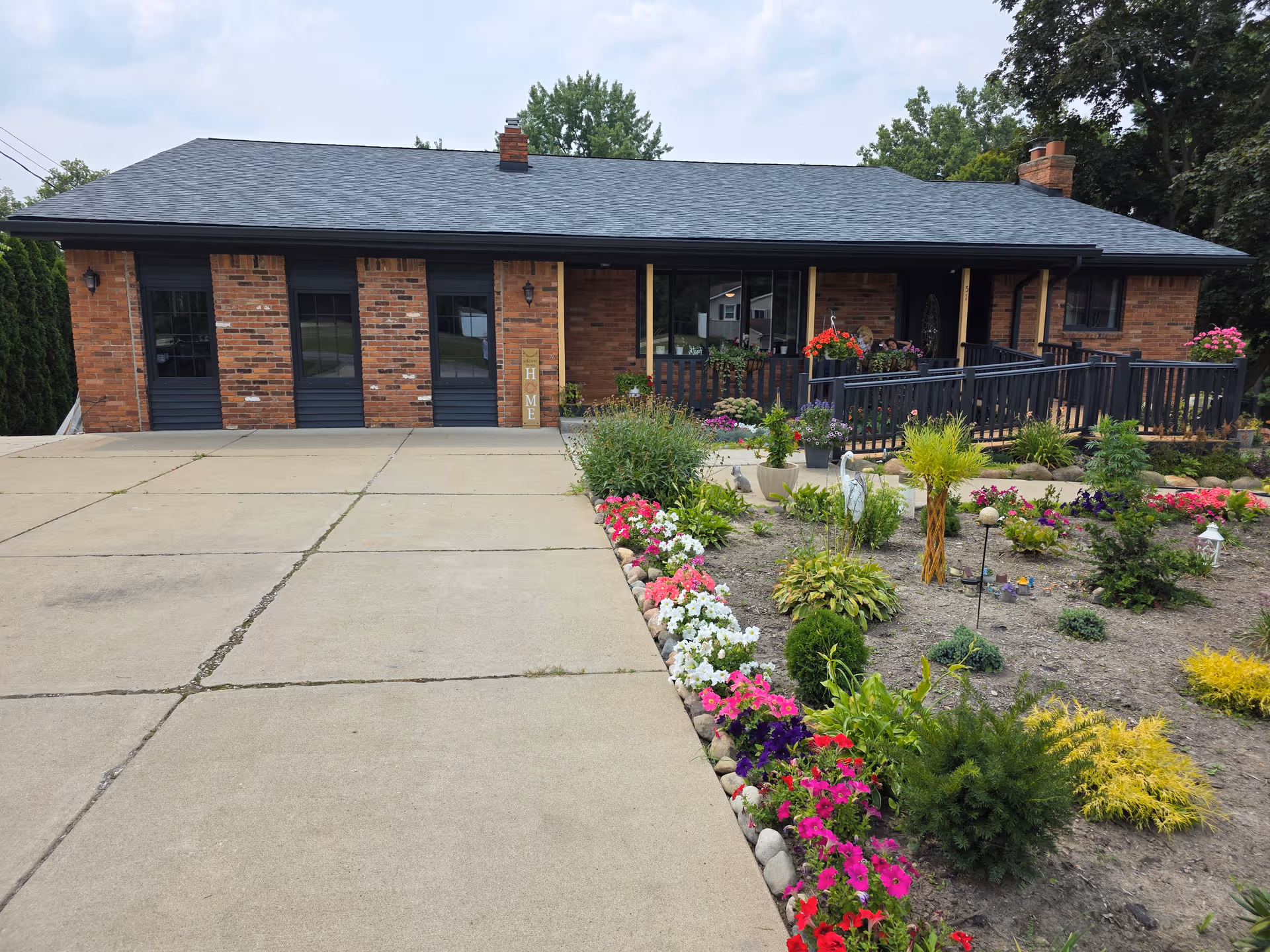 Brick senior living facility with a dark roof, front entrance, and colorful garden along the walkway.