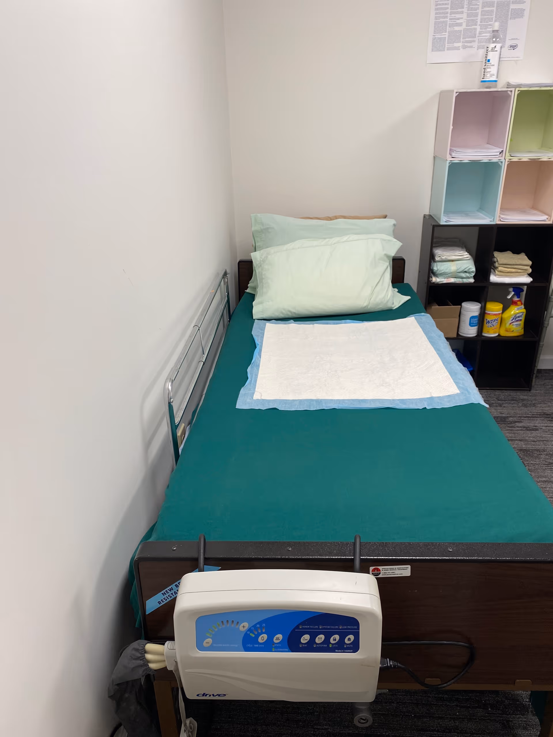 Small senior care bedroom with a green bed, pillows, and cubby storage shelves.