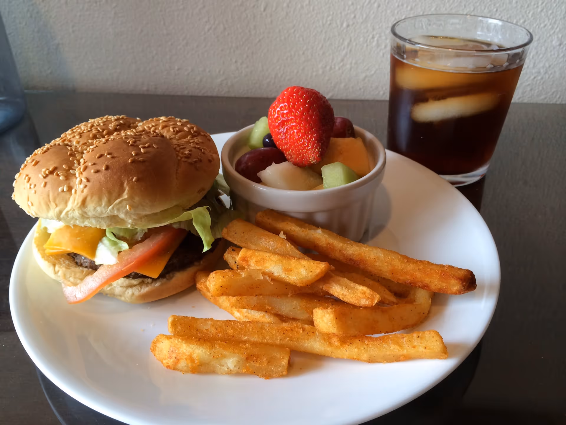 Hamburger with lettuce and cheese, fries, fruit cup, and iced tea on a white plate