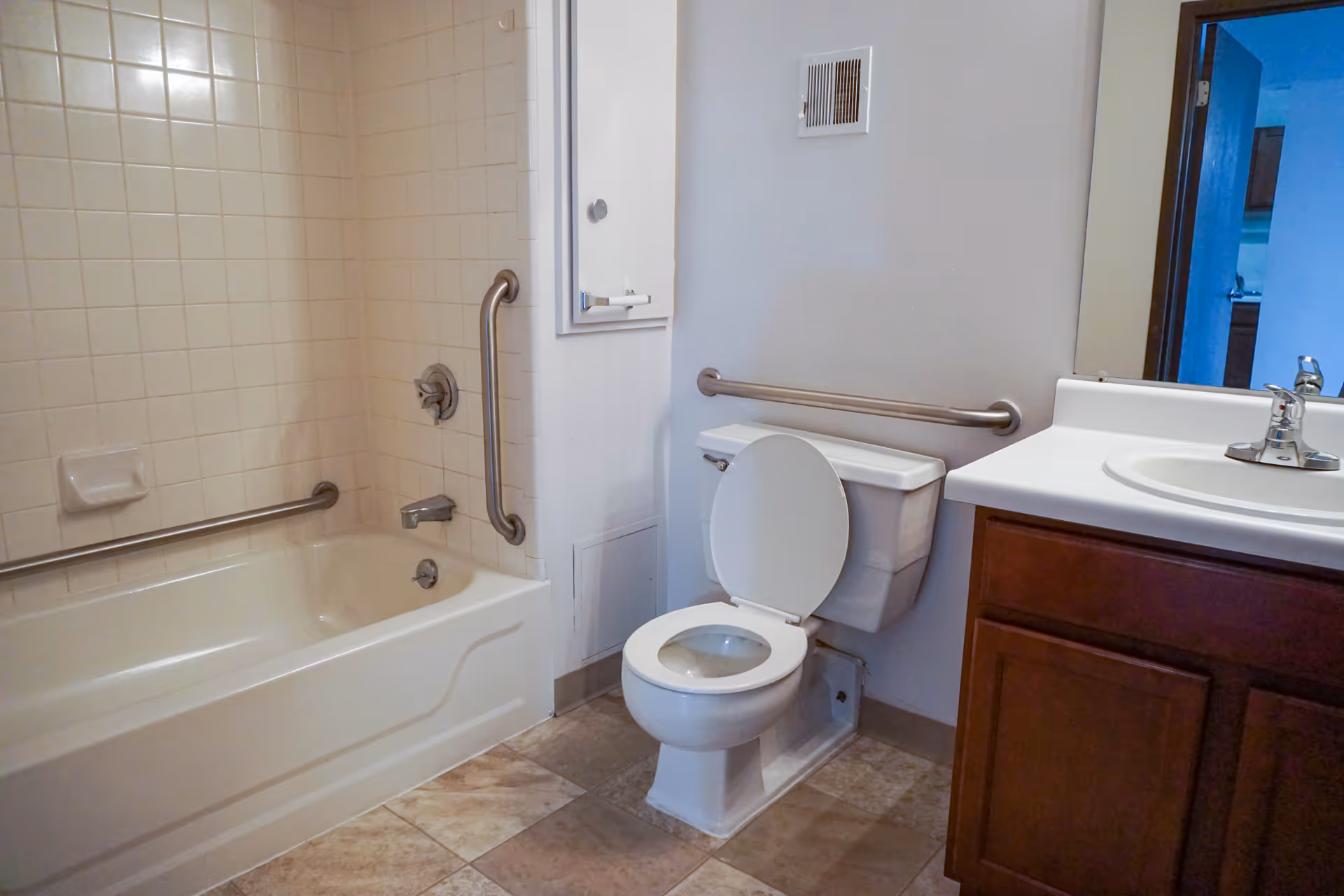 Accessible bathroom with tub, toilet, sink, and grab bars in a senior living unit.
