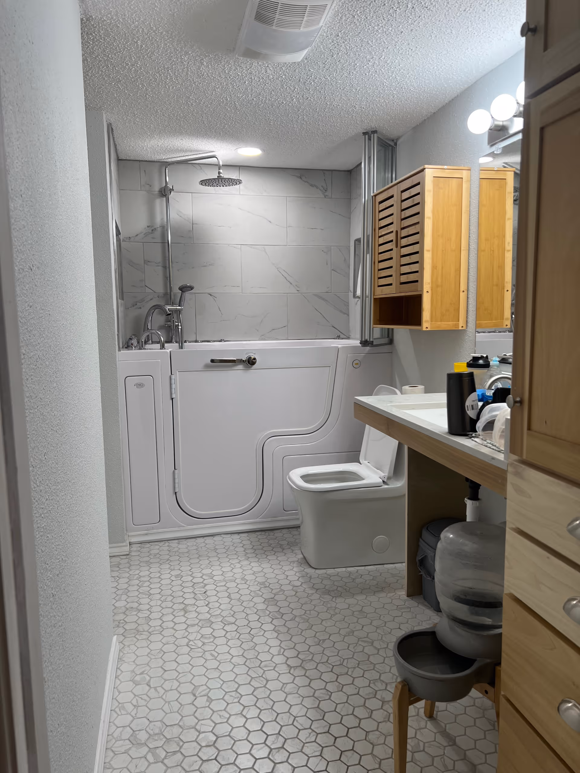 Accessible bathroom with a walk-in tub, toilet, sink, and wooden cabinetry.