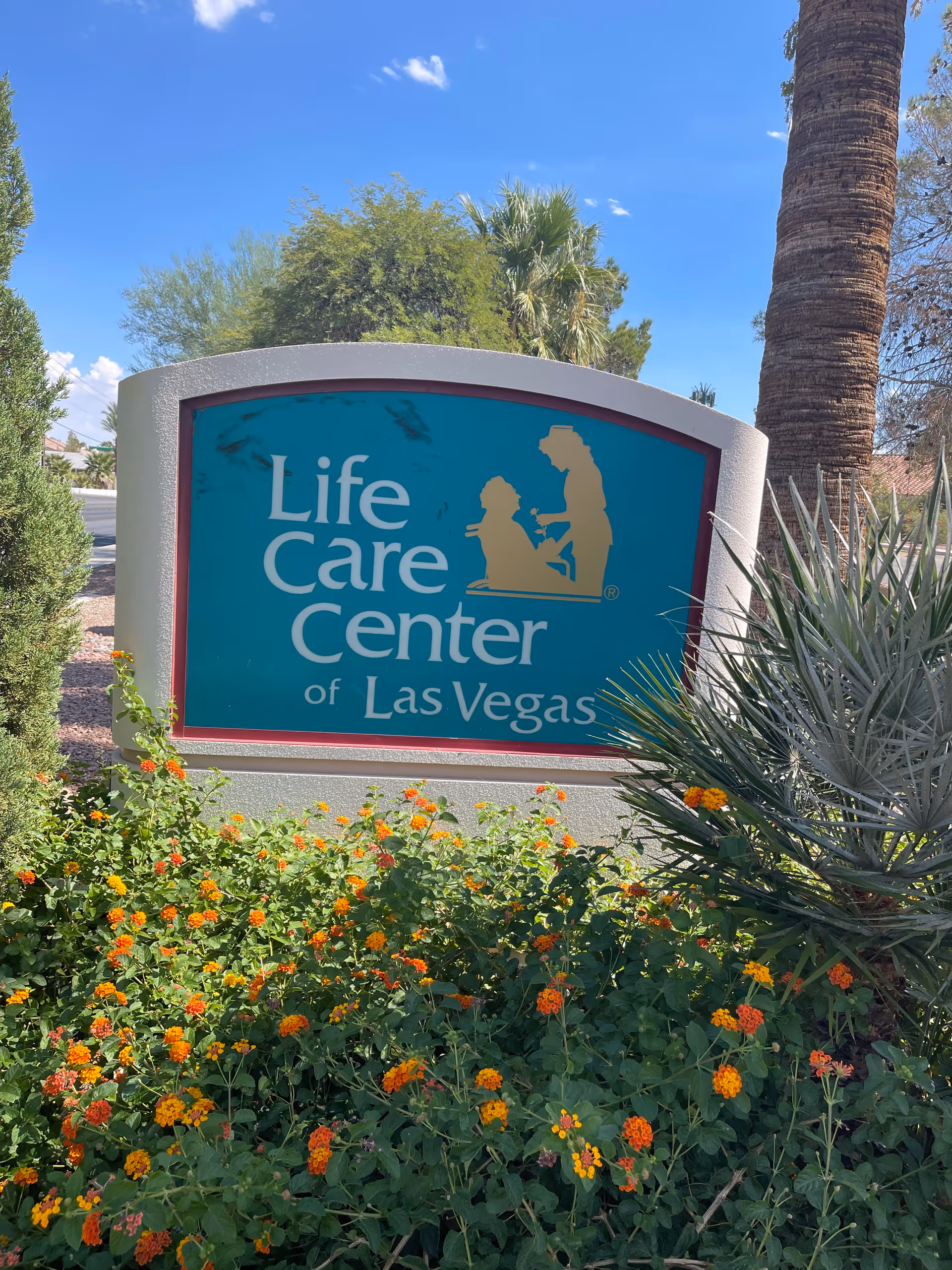 Exterior sign reads Life Care Center of Las Vegas surrounded by flowers.