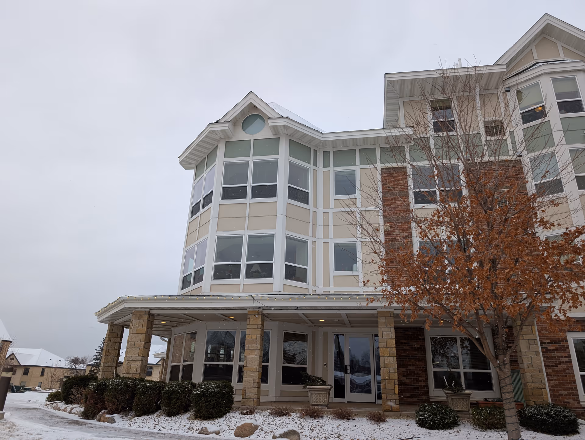Front exterior of a multi-story senior living building with large windows, stone columns, and a snowy entrance.