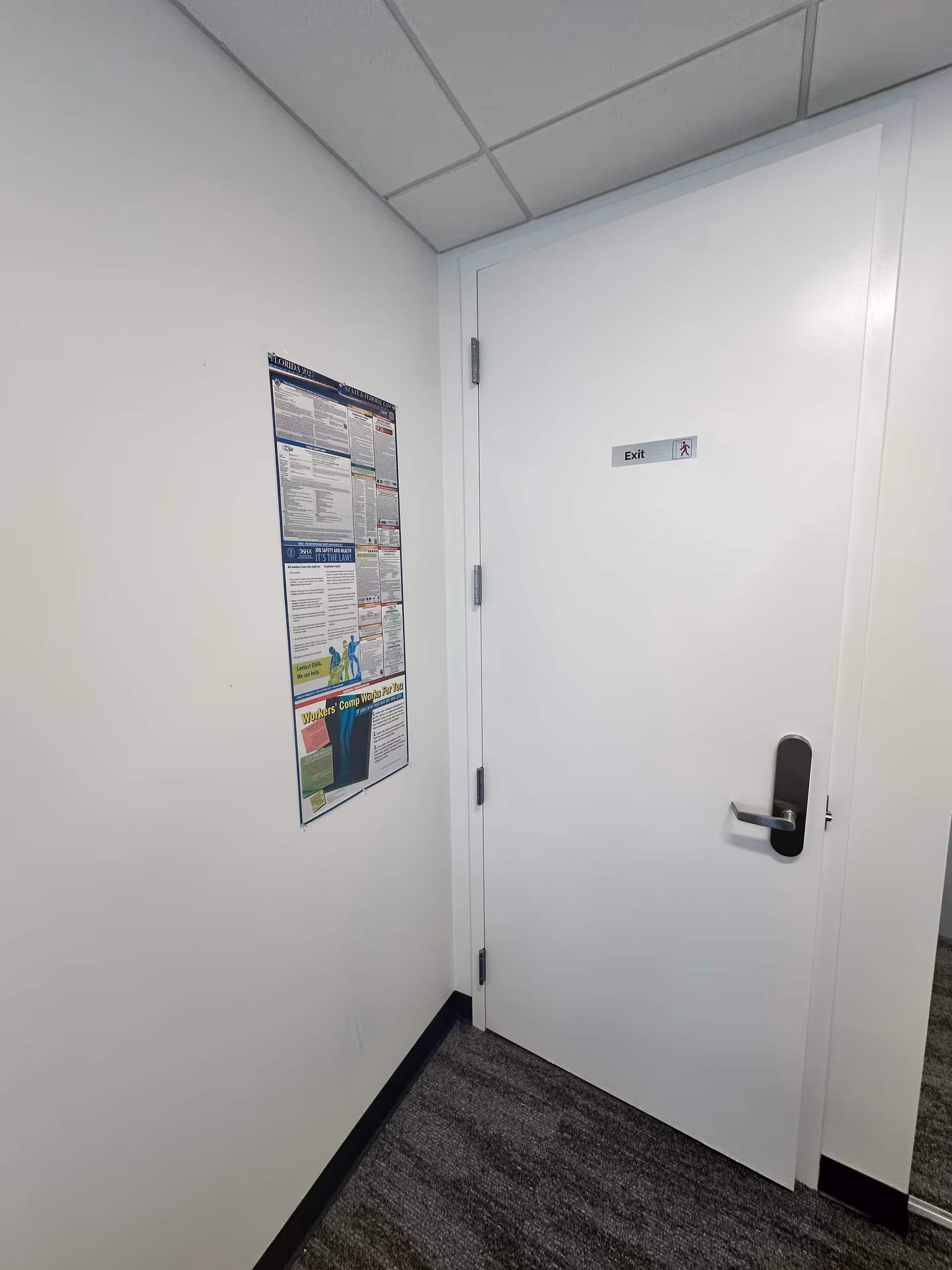 Interior hallway of a facility with an exit door and wall poster.