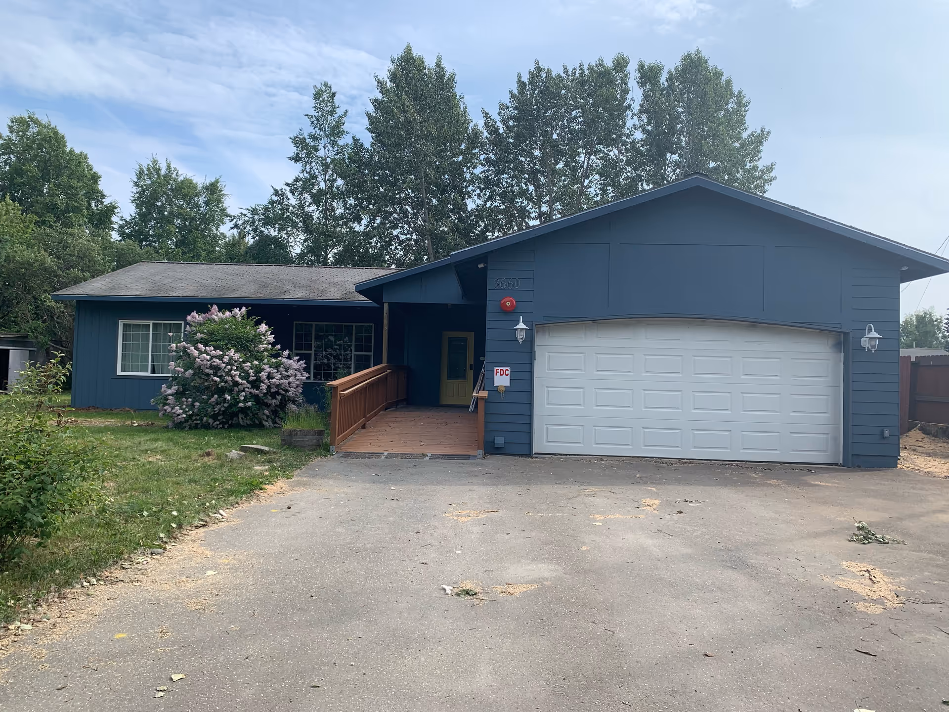 Blue single-story facility with attached garage, front entrance ramp, driveway, and surrounding trees.