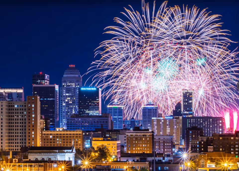 Fireworks exploding over a downtown city skyline at night.