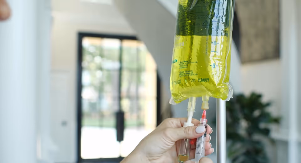 A hand holds an IV bag and syringe inside a bright modern interior.