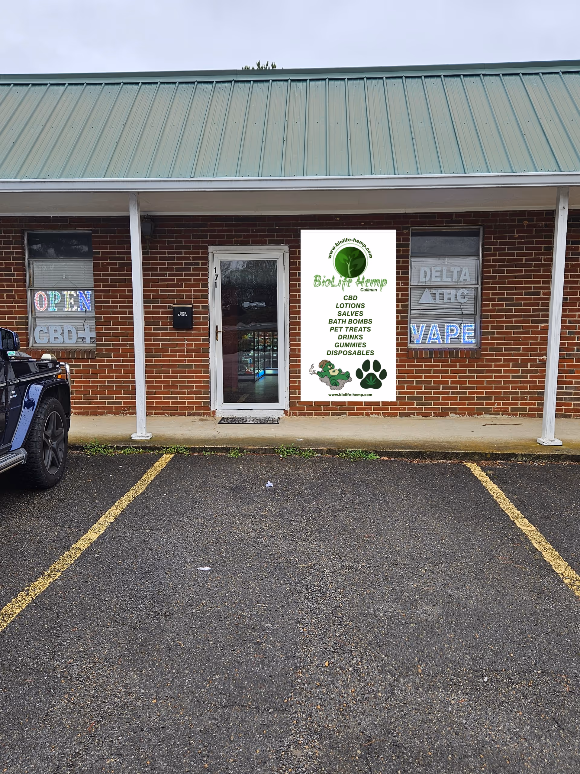Brick storefront with a green metal roof, glass door, and hemp CBD banner.