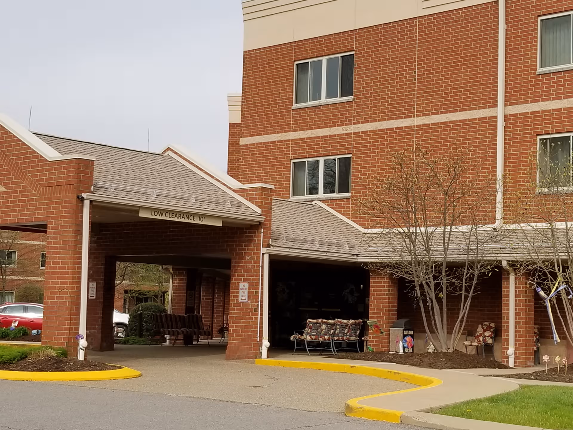 Brick senior living facility entrance with covered drop-off and seating area.
