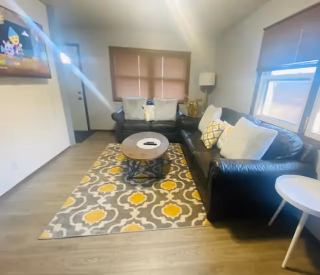 Cozy living room with two black leather sofas, a patterned rug, and a round coffee table.