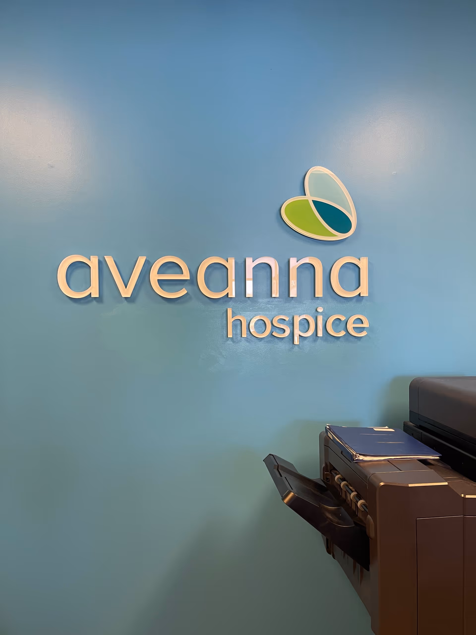 Blue wall with Aveanna Hospice logo and a copier on the right.