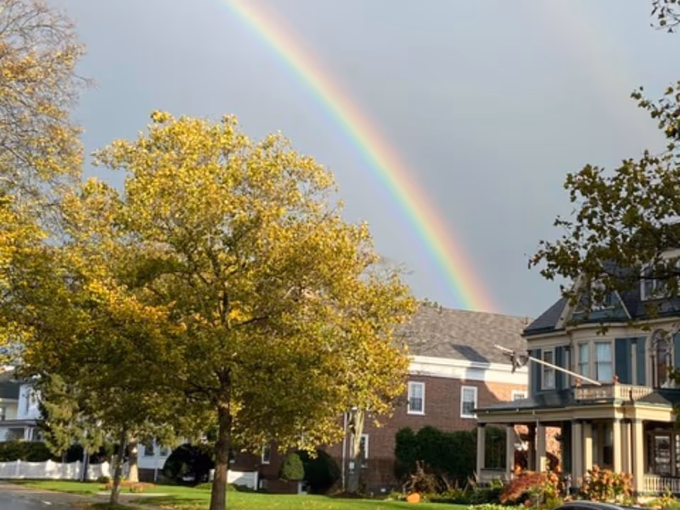 Exterior of Lynn Home for Elderly Persons with a rainbow over autumn trees and front porch.