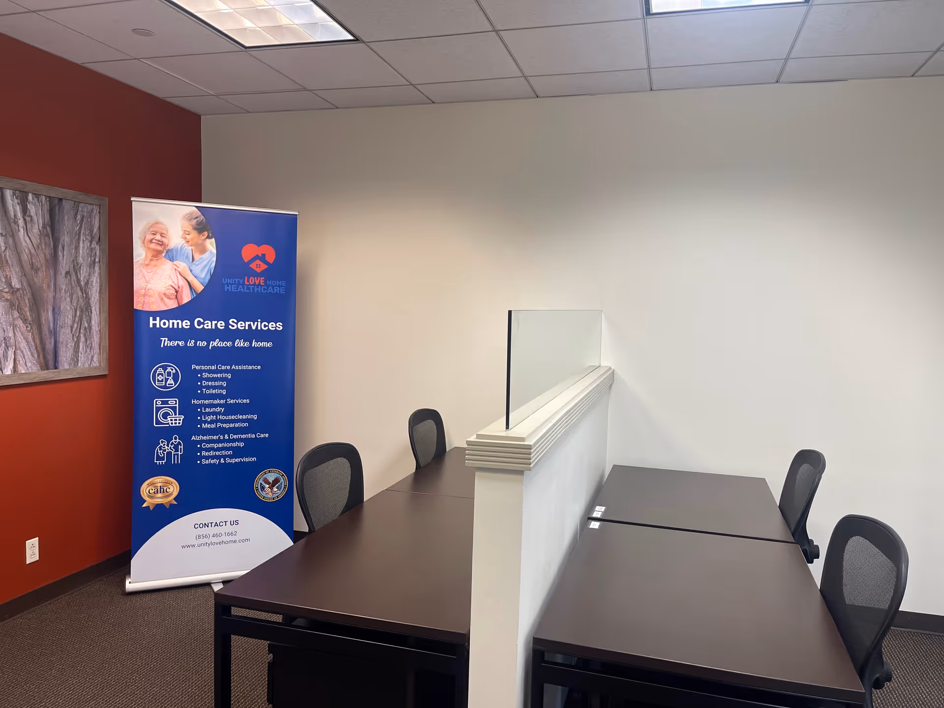 Office-style room with dark wood desks, chairs, and a blue Unity Love Home Care banner.