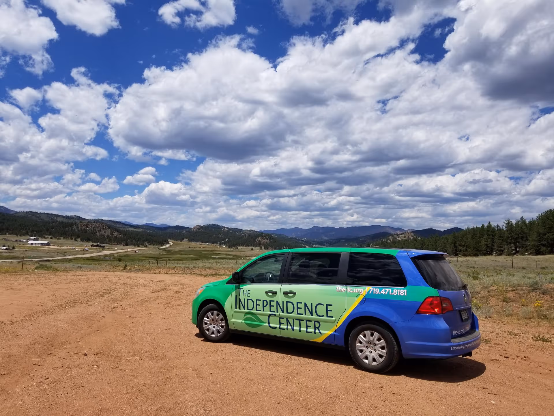 A green and blue van labeled The Independence Center parked on a dirt lot outdoors.