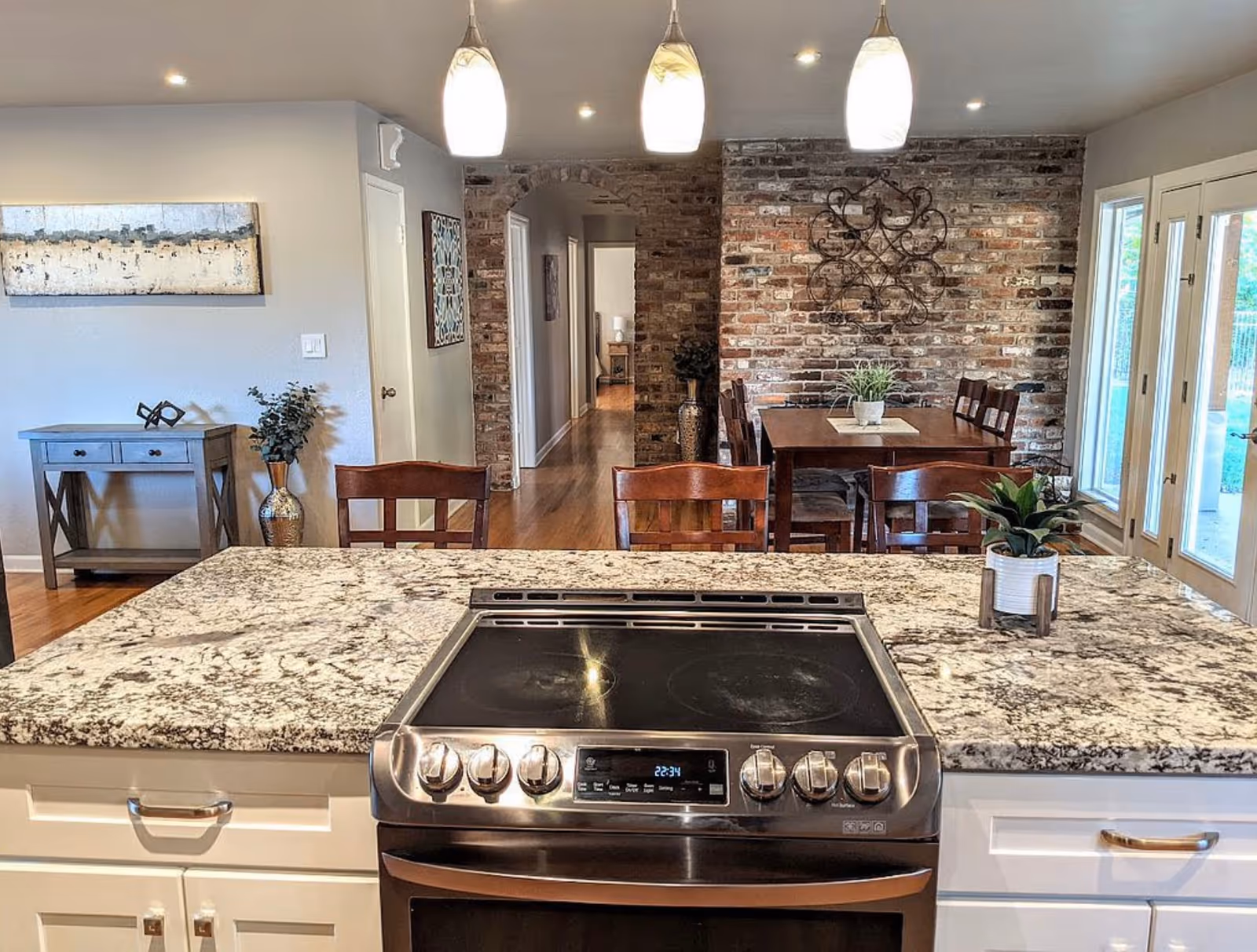Open-concept kitchen with granite island overlooking brick dining area and hallway.