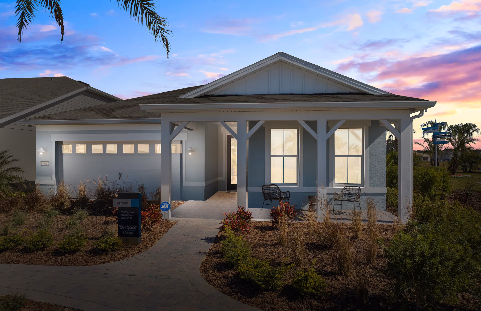 Front exterior of a single-story house with a covered porch, garage, and landscaped path at sunset.