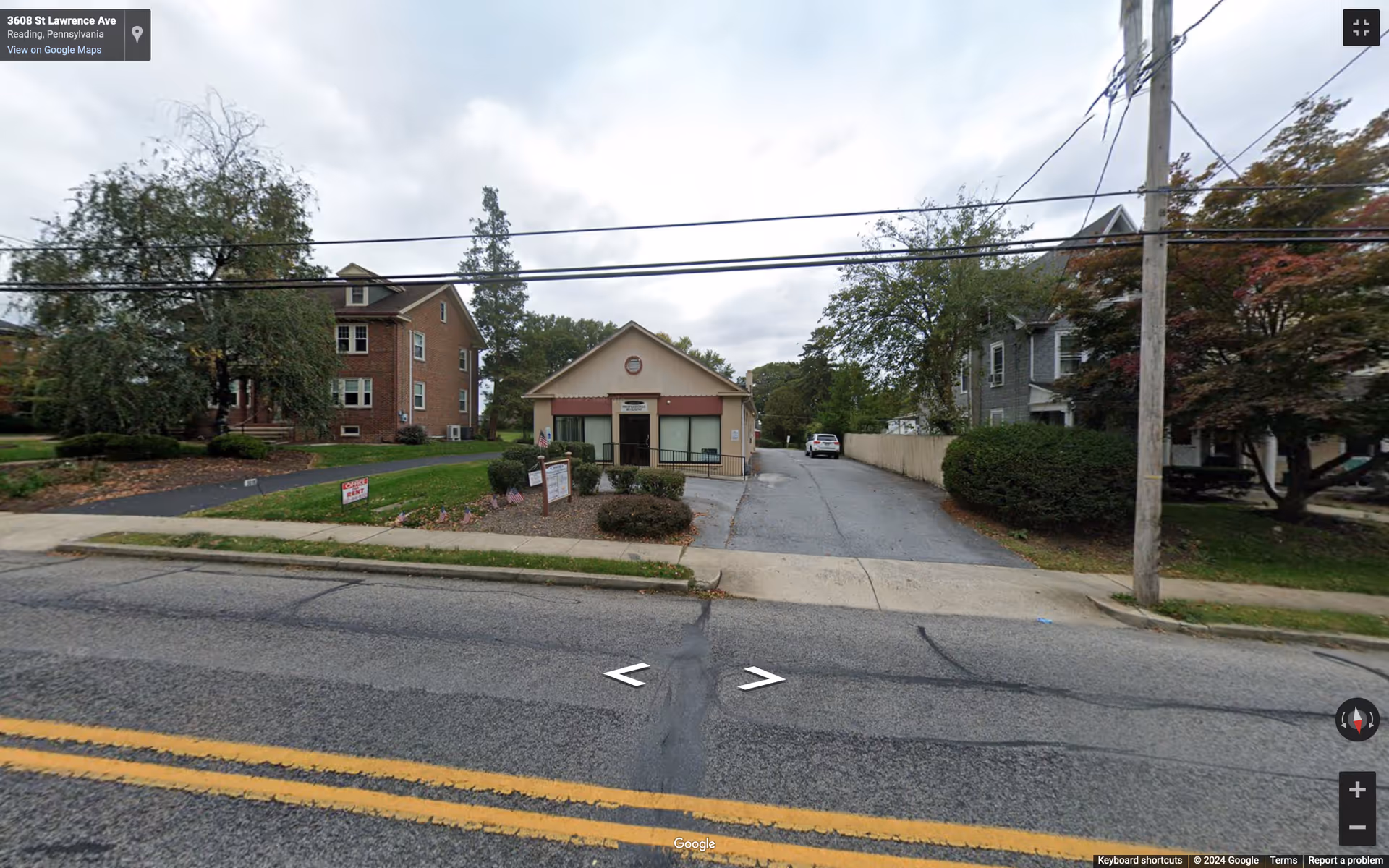 Front view of a small beige senior living facility with driveway and trees.