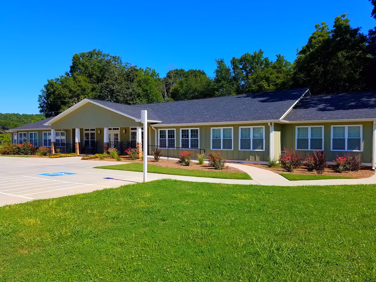 Front exterior of a single-story senior living facility with green siding and landscaped grounds.