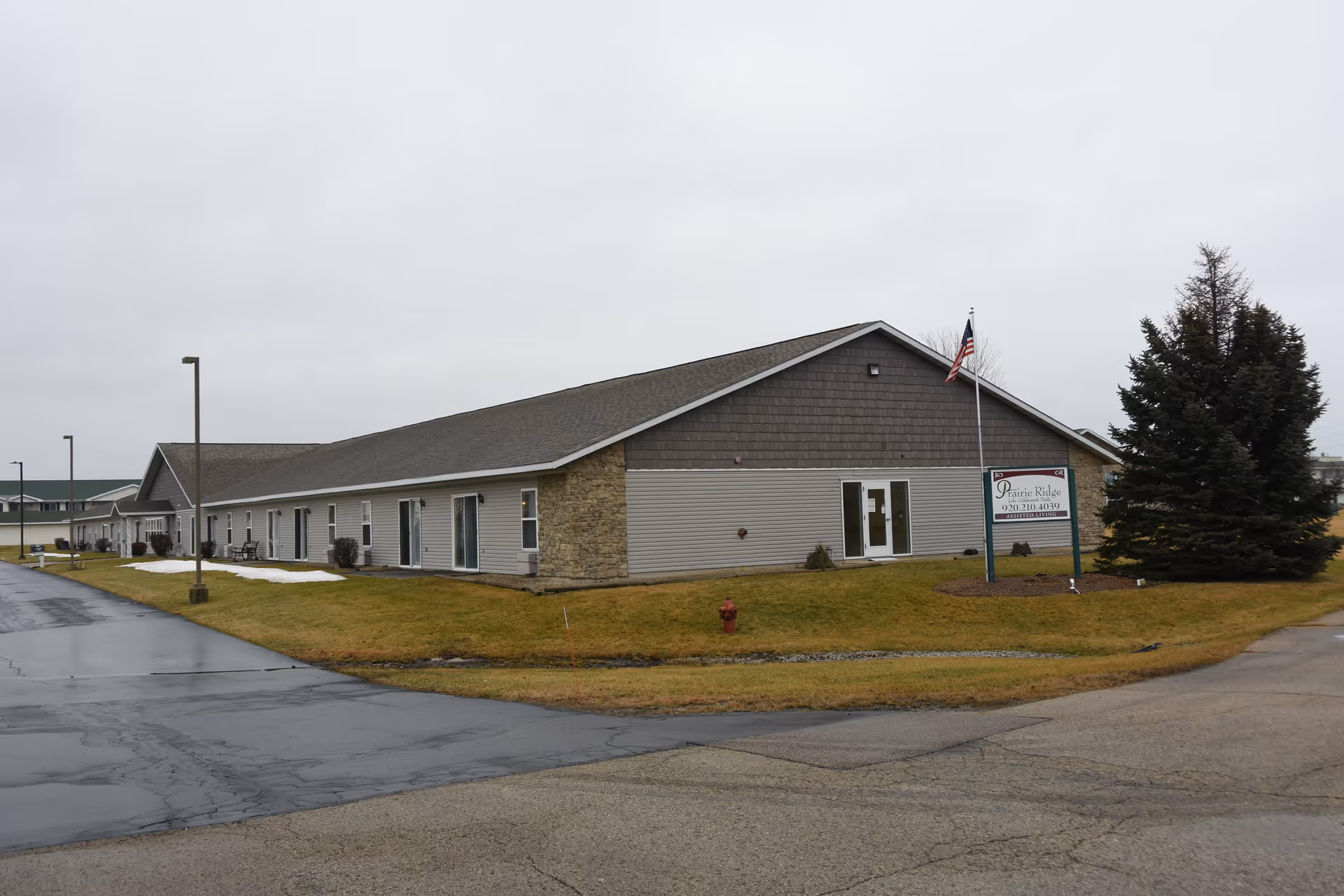Single-story Prairie Ridge assisted living building with gray siding, peaked roof, and an entrance sign.