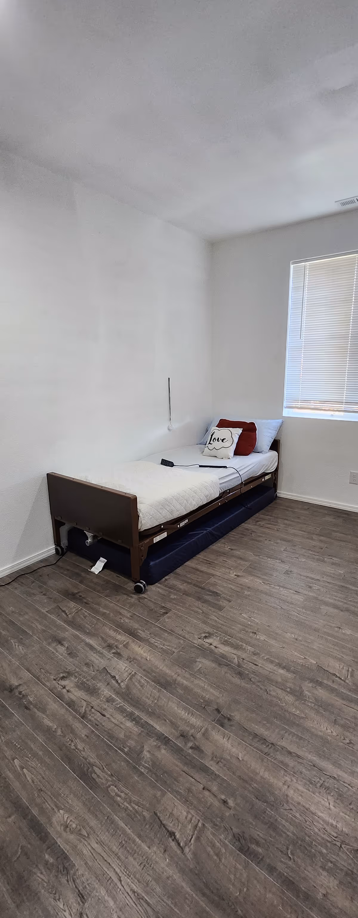 A small bedroom with a single bed, white walls, and a window with blinds.