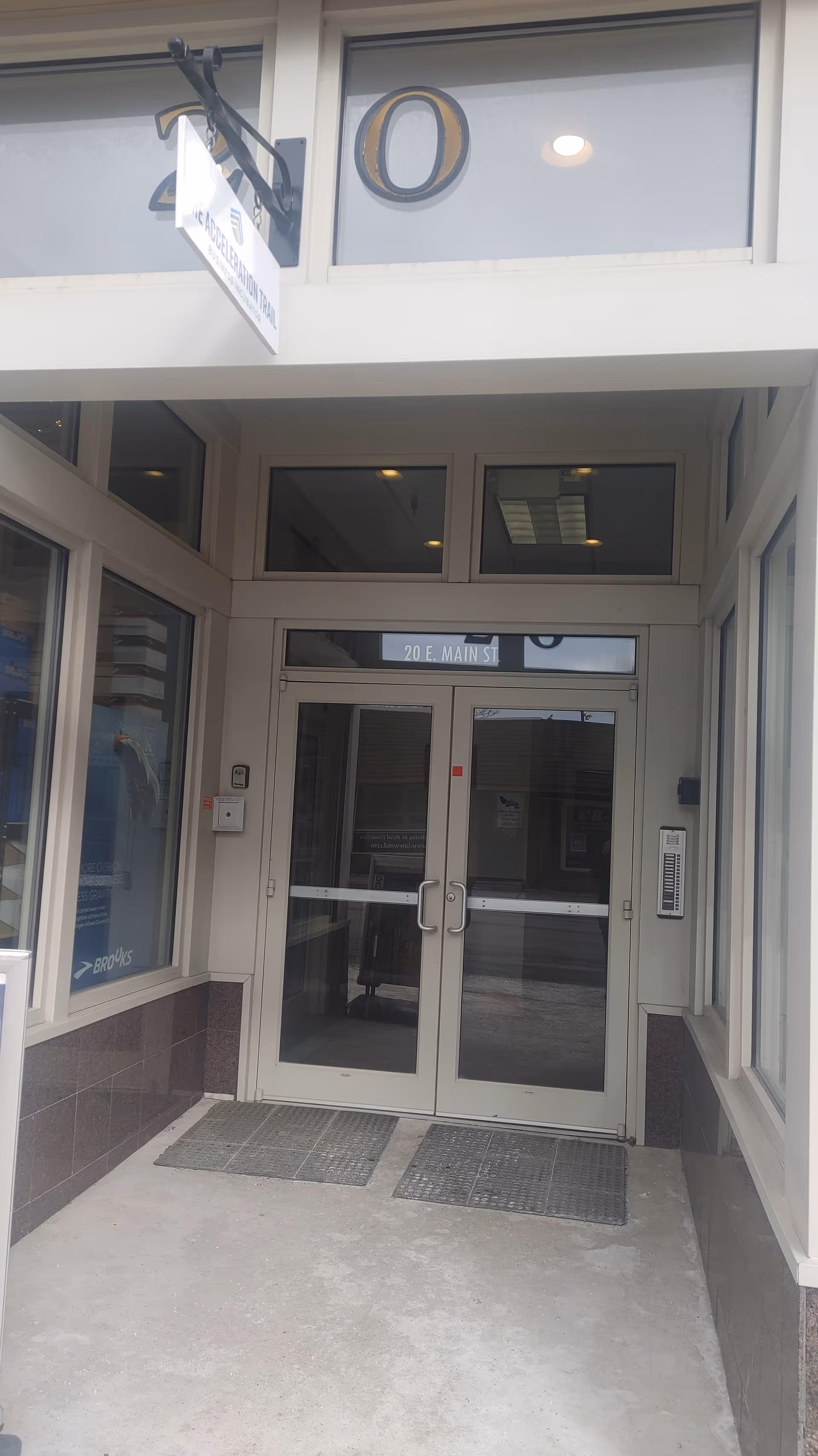 Exterior entrance featuring double glass doors and a street address sign above.