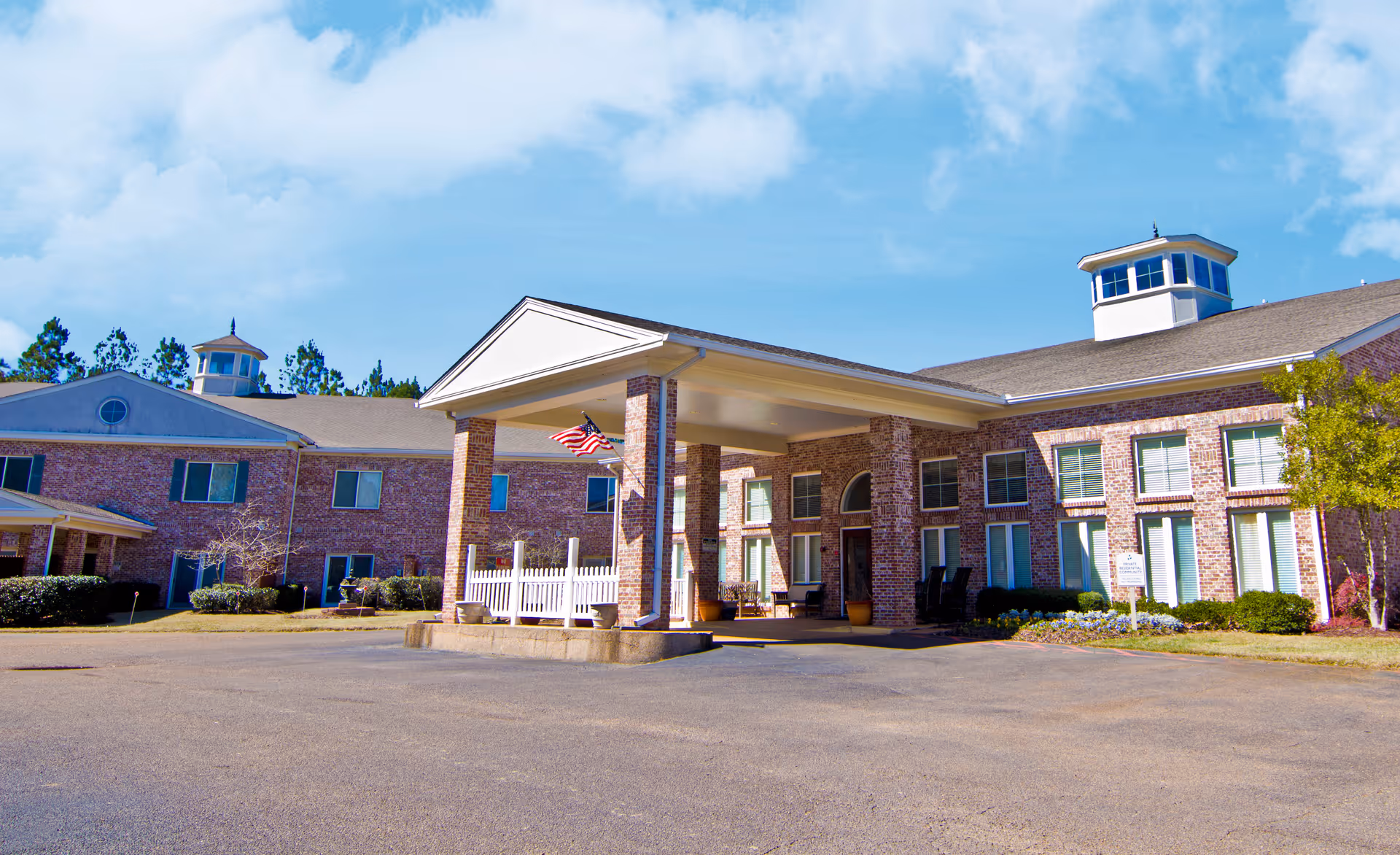Castlewoods Place senior living facility exterior with brick facade, covered entrance, and flag.